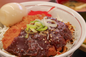 Miso katsudon rice bowl topped with crispy breaded pork cutlet, glossy dark miso sauce, and sliced green onions.
