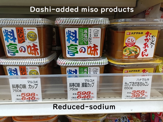 Japanese dashi-added miso products displayed on a supermarket shelf, including regular and reduced-sodium varieties.