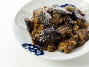 Japanese stir-fried eggplant coated in a rich miso-based sauce, served on a patterned white plate.