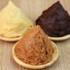 Three varieties of Japanese miso paste in small wooden dishes, showing pale yellow, light brown, and dark reddish-brown colors.