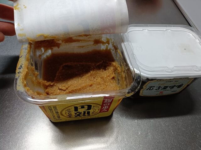 An opened container of Japanese miso covered with an inner sheet, showing how miso is stored after opening and how its surface can darken over time.