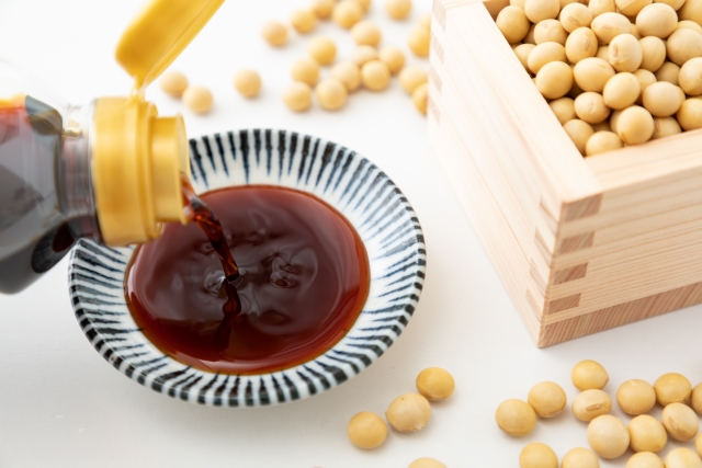 Pouring tamari soy sauce into a small dipping dish beside soybeans