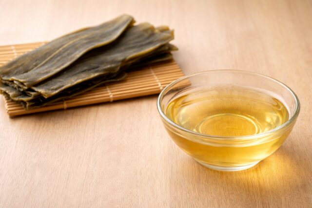 clear kombu dashi broth in a glass bowl with dried kombu behind it