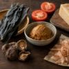 Umami-rich ingredients including kombu, dried shiitake mushrooms, miso, tomatoes, aged cheese, and katsuobushi arranged on a wooden table.