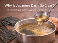 Clear Japanese dashi broth being ladled from a pot with kombu and katsuobushi ingredients beside it