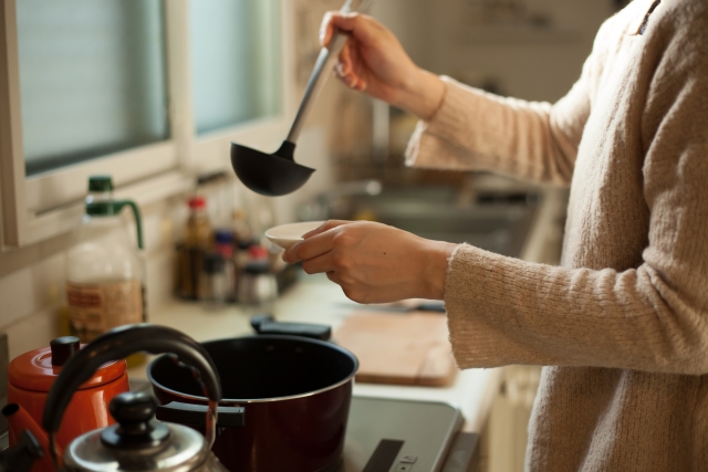 A home cook serving soup into a small bowl while adjusting the flavor in a Japanese kitchen.