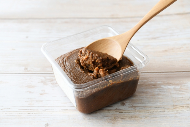 brown Japanese miso paste in a container with a wooden spoon
