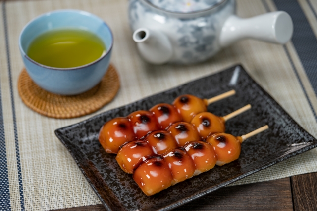 A cup of Japanese green tea with a kyusu and mitarashi dango on a table