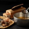 Traditional Japanese dashi ingredients including kombu, katsuobushi, niboshi, and dried shiitake with a pot of freshly made dashi broth