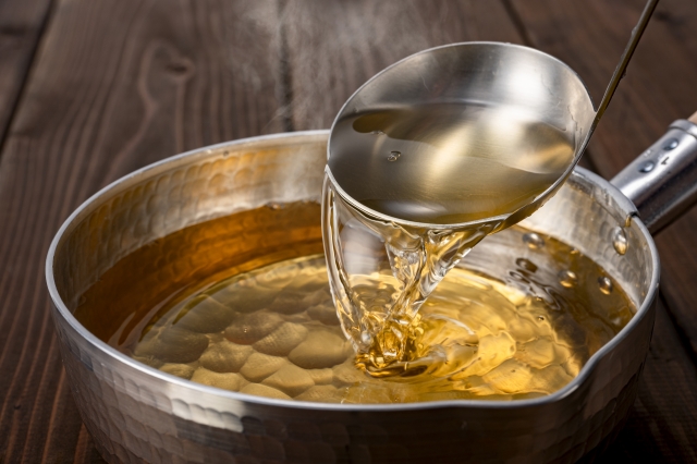 Clear golden dashi broth being poured from a ladle into a pot