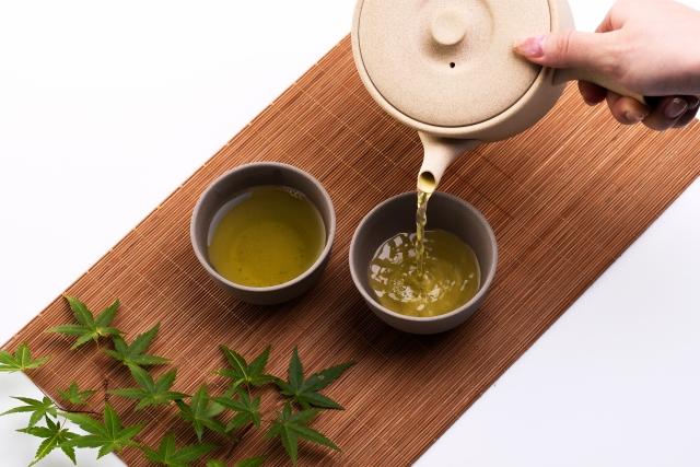 Japanese green tea being poured from a teapot into two teacups