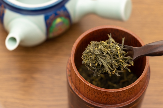 Loose Japanese green tea leaves measured with a small wooden tea scoop