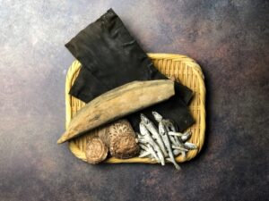 Japanese umami-building ingredients including kombu, katsuobushi, niboshi, and dried shiitake mushrooms on a bamboo tray.