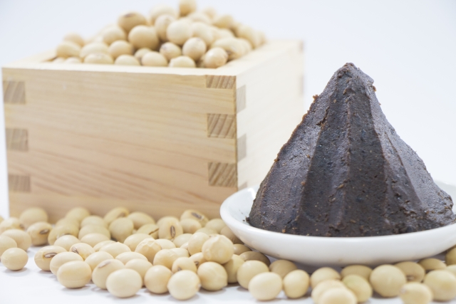 Dark mame miso served beside whole soybeans in a wooden masu box.