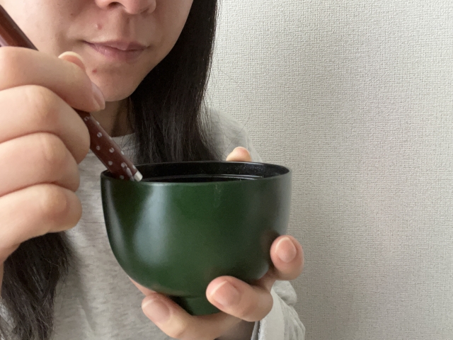 A woman tasting a light soup from a small bowl at home.