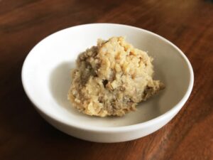 Japanese barley miso in a small white bowl, showing its coarse texture and visible grain pieces.