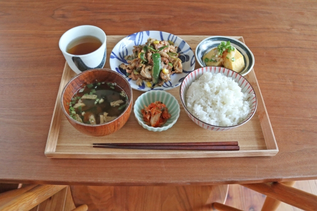 A Japanese home-style meal with rice, miso soup, a main dish, kimchi, and small side dishes served on a wooden tray.