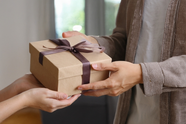 Person handing over a neatly wrapped gift box with ribbon in Japan