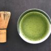 Matcha tea and bamboo whisk on a dark background showing smooth green surface