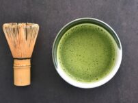 Matcha tea and bamboo whisk on a dark background showing smooth green surface