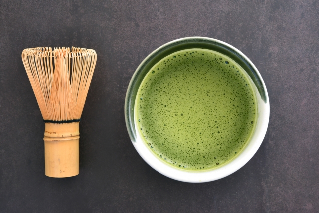 Matcha tea and bamboo whisk on a dark background showing smooth green surface