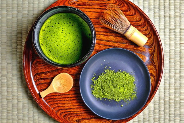 Matcha bowl with foam and powdered tea on a tray with whisk and scoop