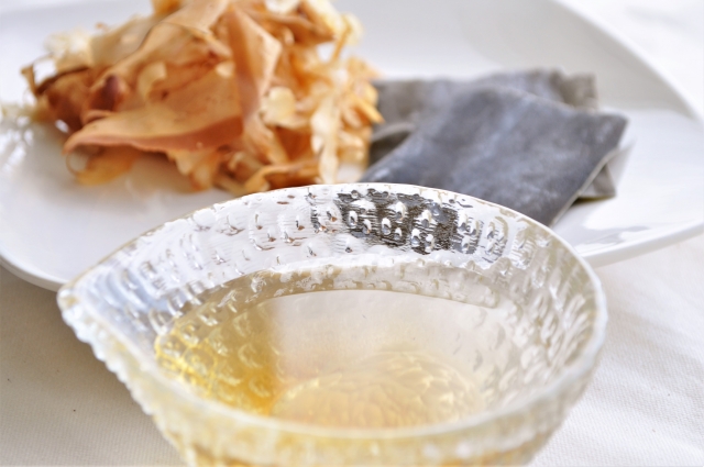 Clear awase dashi in a glass bowl with kombu and shaved katsuobushi in the background.