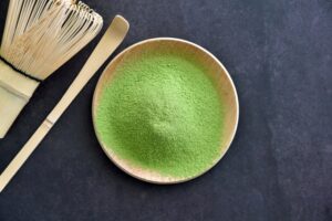 Matcha green tea powder with a bamboo whisk and tea scoop.