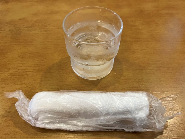 Disposable oshibori in plastic packaging with a glass of water