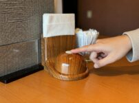 Finger pressing a wooden call button on the table inside a Japanese restaurant