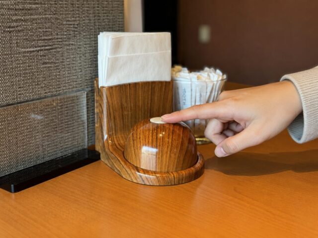 Finger pressing a wooden call button on the table inside a Japanese restaurant