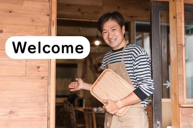Japanese shop owner smiling and welcoming customers at the entrance of a small restaurant