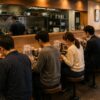 People quietly enjoying ramen at individual counter seats in a modern Japanese restaurant, each spending the meal in their own way.