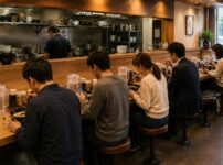 People quietly enjoying ramen at individual counter seats in a modern Japanese restaurant, each spending the meal in their own way.