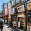 Japanese restaurant street in Tokyo with specialized eateries, including ramen, soba, tonkatsu, and unagi shops, each displaying distinct signs and traditional noren curtains on a bright sunny day.