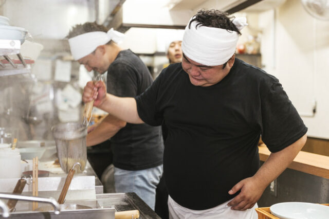 A ramen chef in a small Japanese specialty restaurant carefully prepares noodles by hand before serving each bowl.