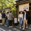 A happy couple leaves a popular Japanese tonkatsu restaurant while other customers continue waiting outside, showing that the experience is about more than just the meal itself.