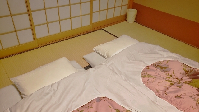 Futons laid out in a Japanese washitsu with tatami flooring and shoji screens, showing how the room transforms into a sleeping space at night
