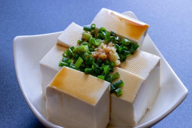 A plate of hiyayakko, chilled tofu topped with chopped green onion, grated ginger, and soy sauce, showing tofu served as a simple dish in Japan.