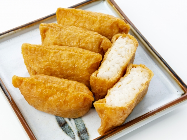 Inari sushi made with seasoned fried tofu pockets filled with white sushi rice, with cut pieces showing the rice inside.
