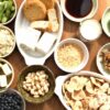 Japanese soybean foods including tofu, natto, miso, kinako, okara, soy milk, edamame, and whole soybeans arranged on a wooden table.
