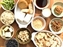 Japanese soybean foods including tofu, natto, miso, kinako, okara, soy milk, edamame, and whole soybeans arranged on a wooden table.
