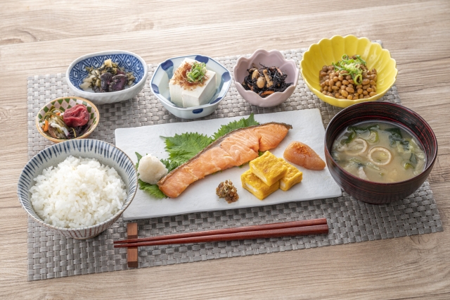 A Japanese breakfast arranged with rice, miso soup, grilled salmon, tamagoyaki, natto, tofu, pickles, and several small side dishes.