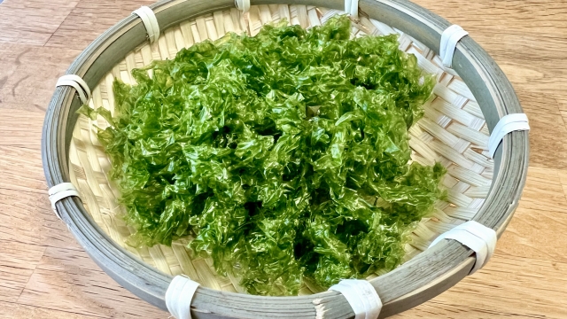 Dried aosa seaweed in thin, irregular green flakes, showing its leaf-like texture.