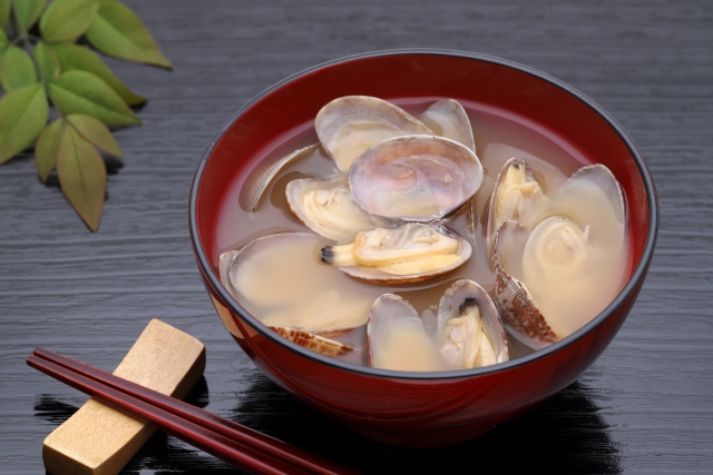 A bowl of clam miso soup with opened clams in a red lacquer bowl.