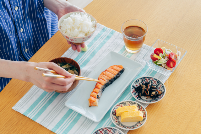 A person eating a balanced Japanese breakfast with rice, grilled salmon, miso soup, tamagoyaki, hijiki, and salad.