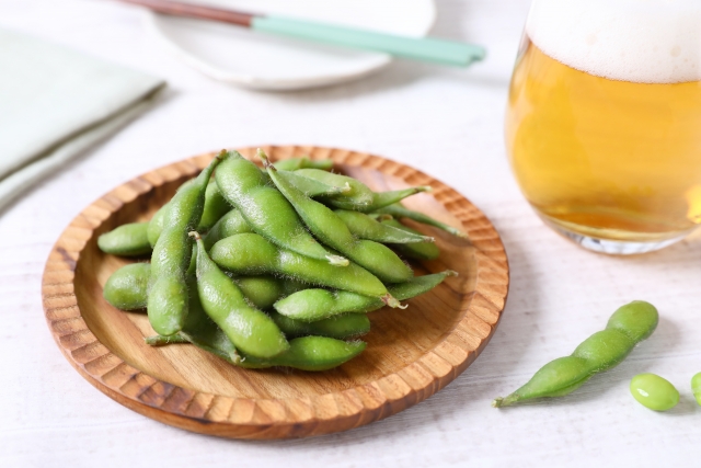 Edamame served on a wooden plate with a glass of beer on a Japanese dining table.