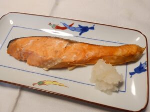 A simple piece of grilled salted salmon with grated daikon, served on a household plate as part of a Japanese breakfast.
