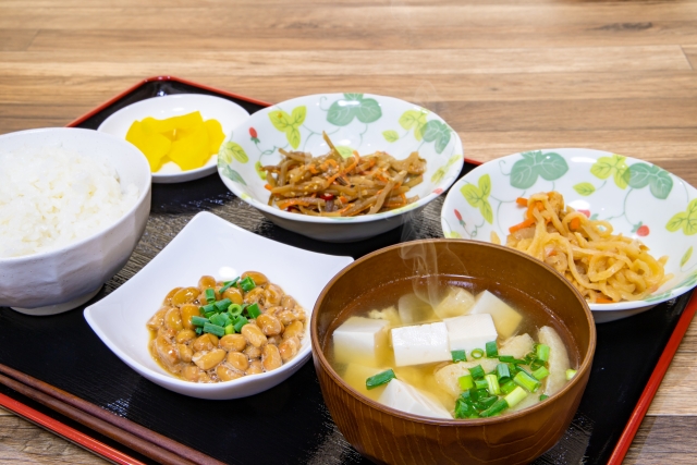 A simple Japanese breakfast tray with steamed rice, tofu miso soup, natto, pickles, and small vegetable side dishes.