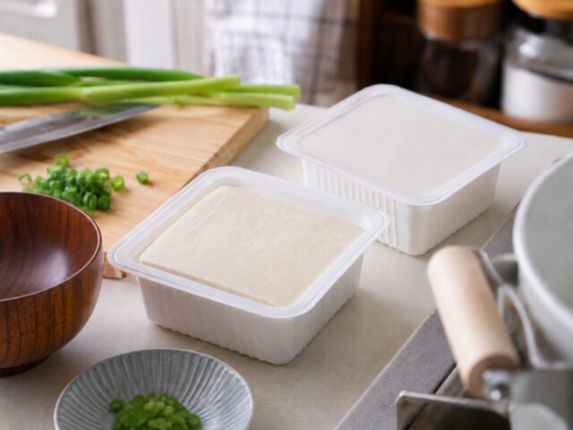 Packaged tofu on a kitchen counter with green onion and cooking tools, showing tofu as a convenient everyday ingredient in Japan.